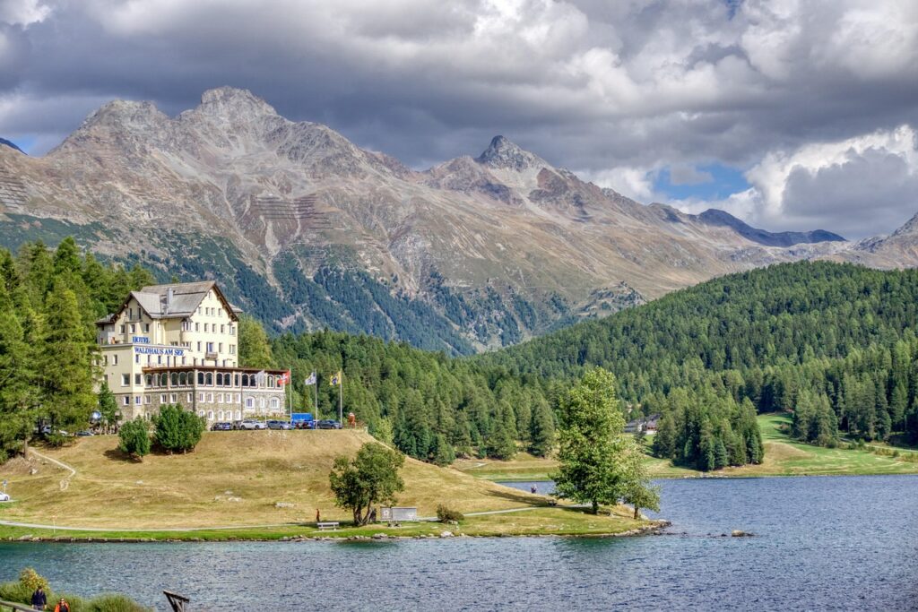 Beautiful view of a Swiss lakeside hotel surrounded by towering mountains and lush green forests, embodying Switzerland’s stunning landscapes and tranquil culture