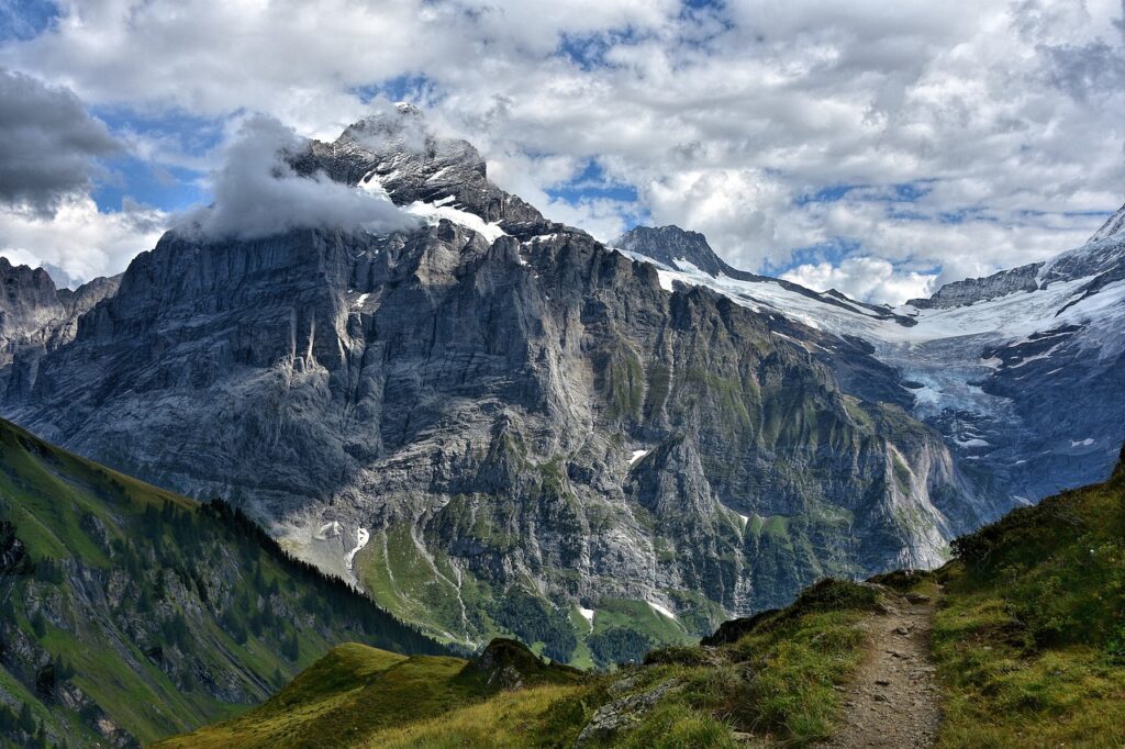 Stunning view of the Swiss Alps with lush green valleys, towering mountain peaks, and a beautiful trail winding through the landscape