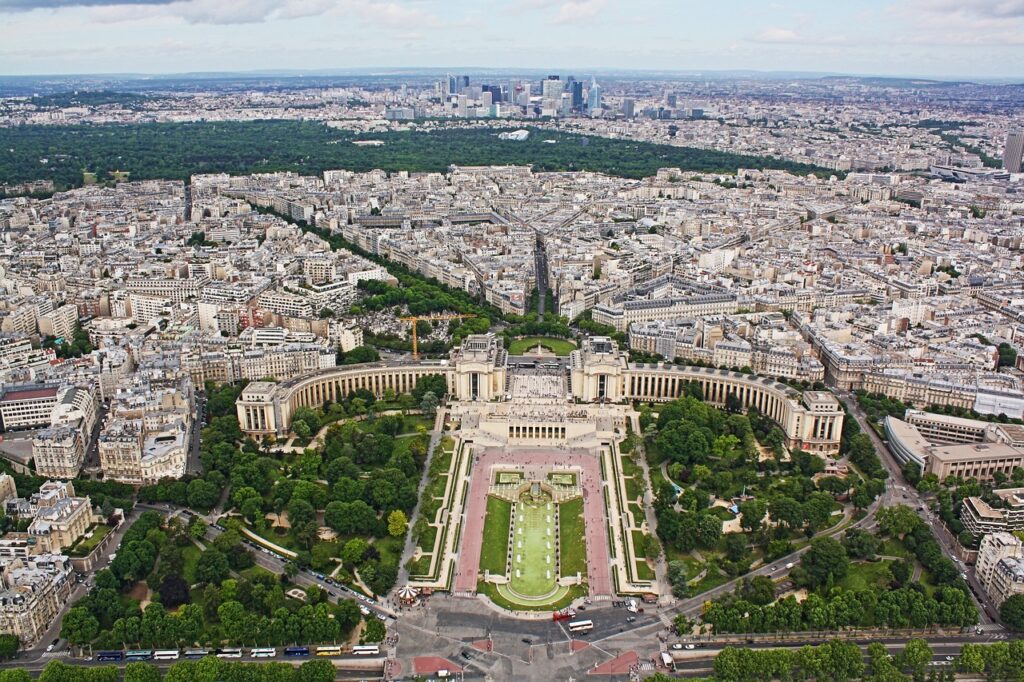 Aerial view of Paris, showcasing the Trocadéro Gardens and the cityscape leading up to the Eiffel Tower, with green spaces and the La Défense skyline in the background.