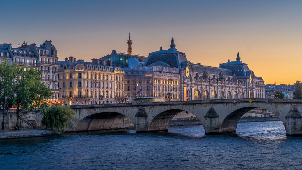 View of the Musée d'Orsay in Paris at sunset, with the Seine River and Eiffel Tower in the background.
