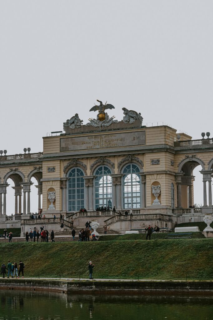 View of the Gloriette at Schönbrunn Palace in Vienna, featuring the golden eagle sculpture and people walking around the landscaped gardens